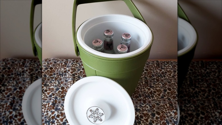 Dört şarap soğutucu şişesinin içine nasıl sığabileceğini gösteren, kapağı kapalı yeşil bir Rubbermaid buz kovası.