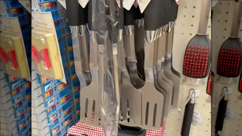 Dollar Tree'deki rafta metal maşa ve ızgara fırçalarının yanında asılı bir ızgara spatulası.