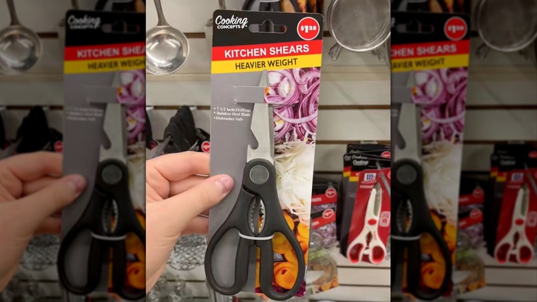 Bir el, Dollar Tree'deki sergi duvarının önünde bir çift Cooking Concepts Mutfak Makası tutuyor.