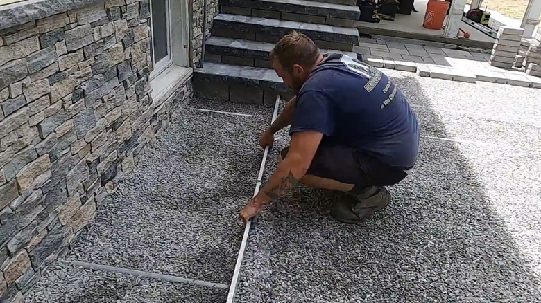 Adam, bir dizi beton blok merdivenin tabanını bitirmek için kırma taşı düzleştiriyor.