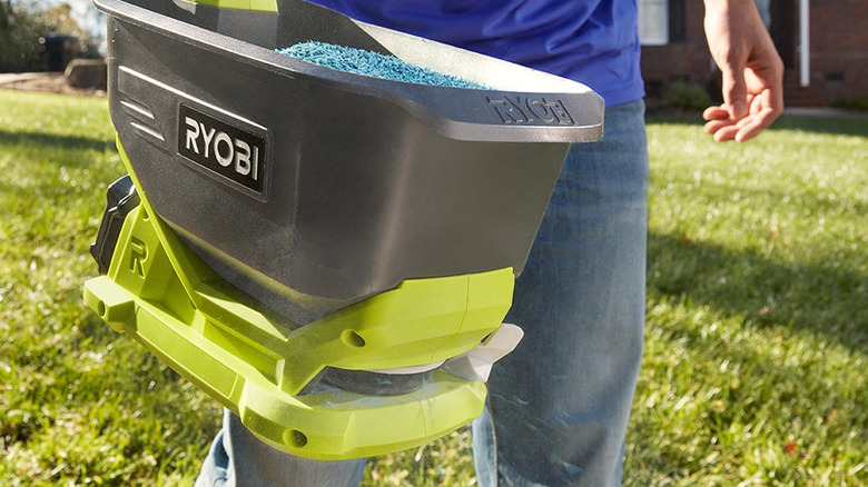 Gübre topaklarını yaymak için Ryobi motorlu serpme makinesi kullanan bir adam