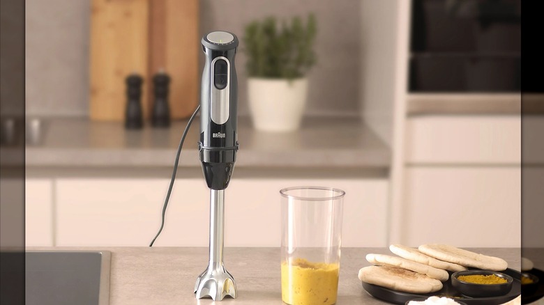 Braun MultiQuick 5 Pro 4'ü 1 Arada Daldırma Blender'ı mutfaktaki bir tezgahın üzerinde bir kavanoz humus ve biraz pide ekmeğinin yanında.