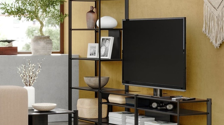 Her rafında süslemeler bulunan, açık raflı JÄTTESTA TV saklama kombinasyonunda bir TV