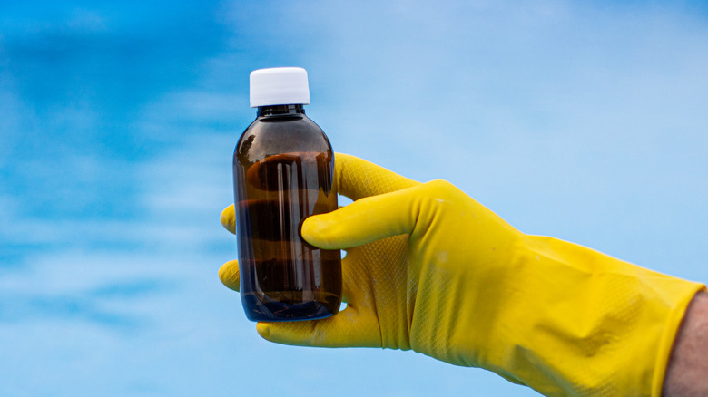 Havuzun önünde sarı eldivenli koyu renkli cam şişe tutan bir kişi.