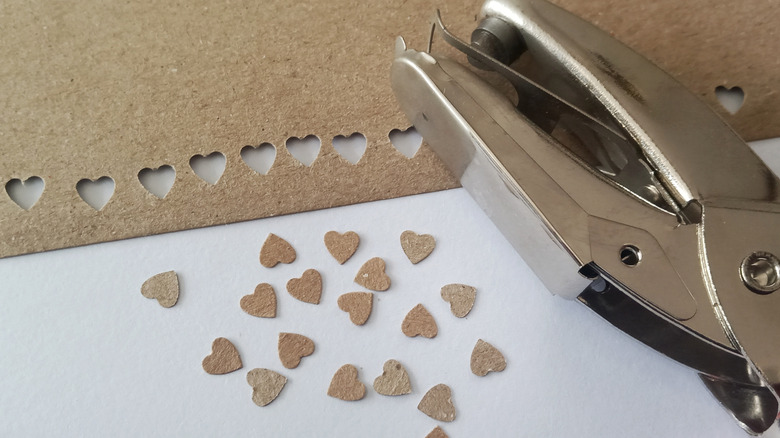 Kahverengi kağıttan kesilmiş minik kalpler masanın üzerinde metal bir delgeçin yanında duruyor.