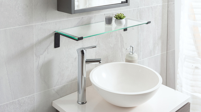 Krom musluklu ve cam raflı yuvarlak banyo lavabosu.