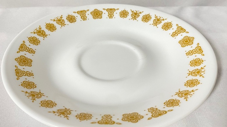 Kelebek Altın Corelle tabağının yakın çekimi, kenarlarında altın çiçekler ve kelebekler desenli beyaz bir tabak.