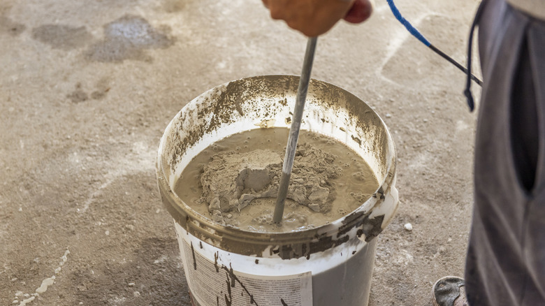 5 galonluk kovada beton tozunu suyla karıştıran kişi. döşeli yüzey