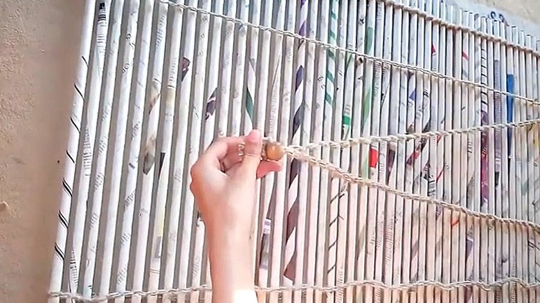 Kişi gazete rulolarından yapılmış DIY perde kordonu için boncuk tutucuyu gösteriyor