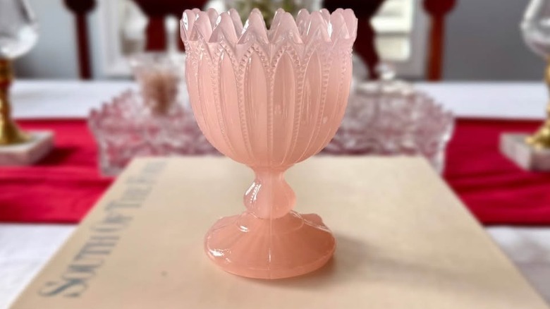 Masanın üzerindeki ciltli kitabın üstüne yerleştirilmiş pembe opalin cam kadeh