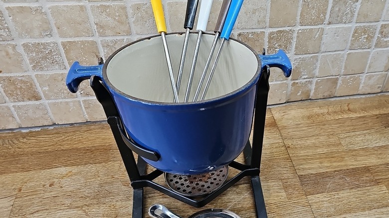Vintage mavi emaye dökme demir Le Creuset fondü seti, seramik arka panelli ahşap mutfak tezgahının üzerinde duruyor.