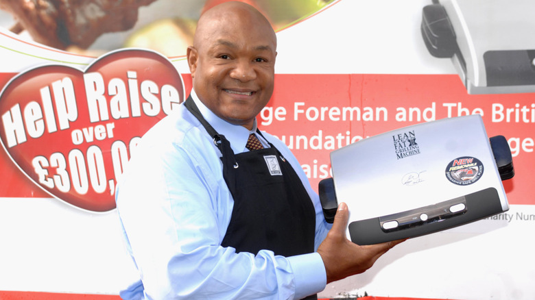 George Foreman bir etkinlikte gülümsüyor ve George Foreman Grill'i tutuyor