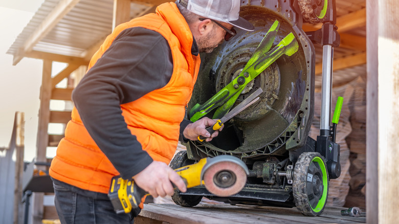 Bir adam, onları keskinleştirmek için aletleri tutarken çim biçme makinesinin bıçaklarını inceliyor