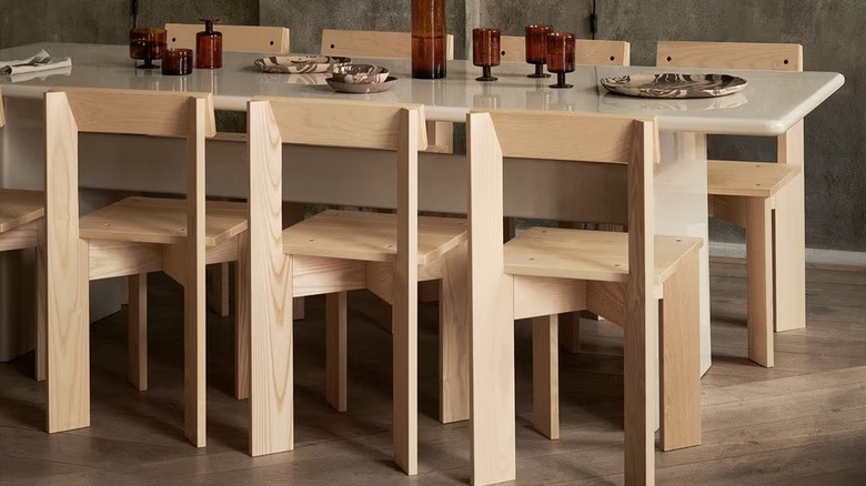 Üzerinde modern sofra takımlarının bulunduğu büyük bir yemek masasının etrafında Ferm Living Ark Yemek Sandalyeleri seti.
