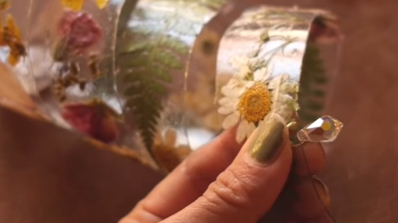 Kendin Yap spiral çiçek güneş yakalayıcı projesinin üzerinde kristal bir boncuk tutan başparmak.