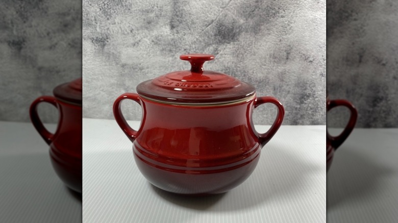 Beyaz ve gri bir arka planda sergilenen kırmızı bir Le Creuset fasulye kabı.