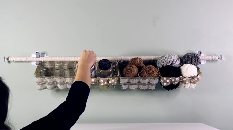 Bir kadın, el işi malzemelerini el işi odasındaki DIY asılı depolama rafına yerleştiriyor.