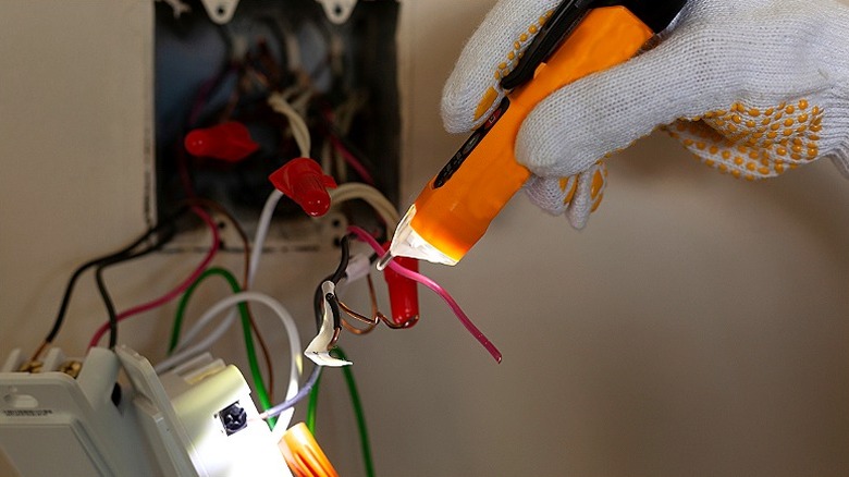 Bir kişinin eldivenli eli duvar panelindeki kabloları test etmek için voltaj test cihazı kullanıyor