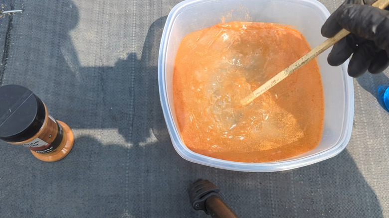 Bir kişi, bahçe bitkileri için haşere kovucu bir sprey yapmak üzere kırmızı biberi beyaz plastik bir kaptaki suya karıştırıyor.