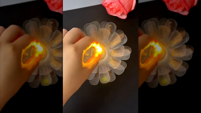Plastik şişe lotus çiçeğine mum yerleştiren kişi
