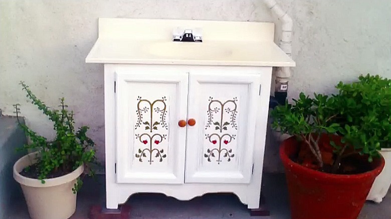 Ön tarafında güzel boyalı bir tasarıma sahip eski bir dolap kullanılarak yapılmış beyaz vintage tarzı bir makyaj masası