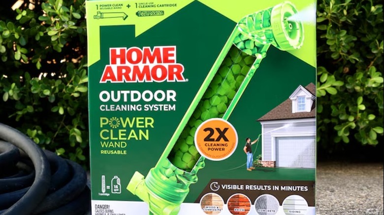 Arka planda hortum ve çalılar bulunan Home Armor elektrikli temizleme çubuğunu içeren kutunun yakından görünümü