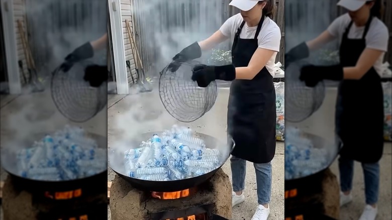 Plastik su şişeleriyle dolu bir ateş çukuru ve yanında duran, elinde tel sepet tutan bir kadın.