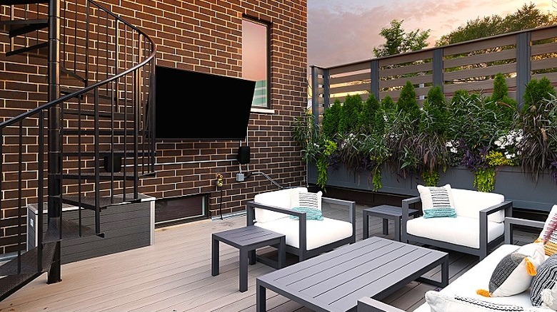 Dışarıda bir tuğla duvara monte edilmiş bir TV ve önünde veranda mobilyası