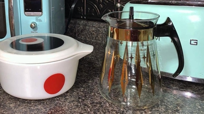 Beyaz ve kırmızı bir güveç kabının yanındaki mutfak tezgahında atomik desenli Pyrex sürahi.