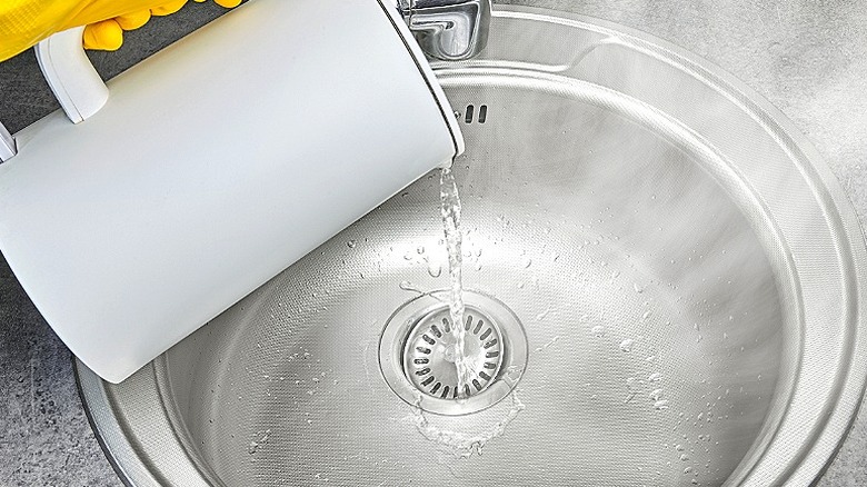 Eldivenli bir el, su ısıtıcısından lavabo giderine kaynar su döküyor