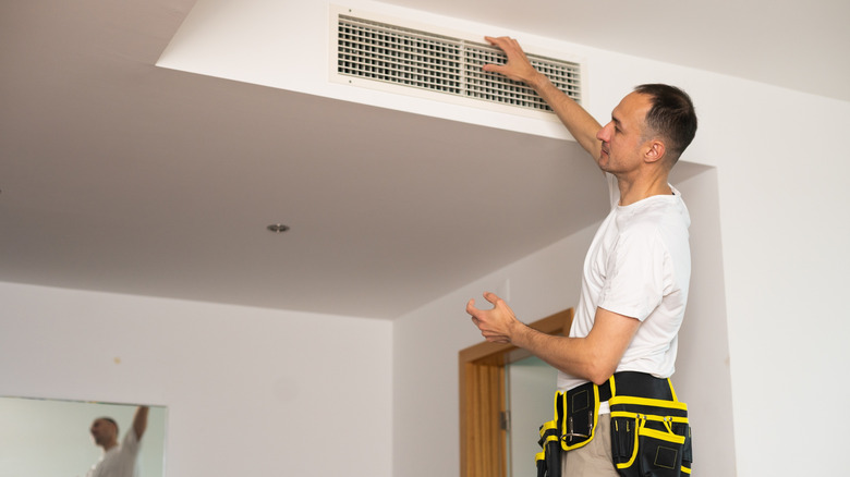 HVAC teknisyeni duvardaki havalandırma deliğini kontrol ediyor.