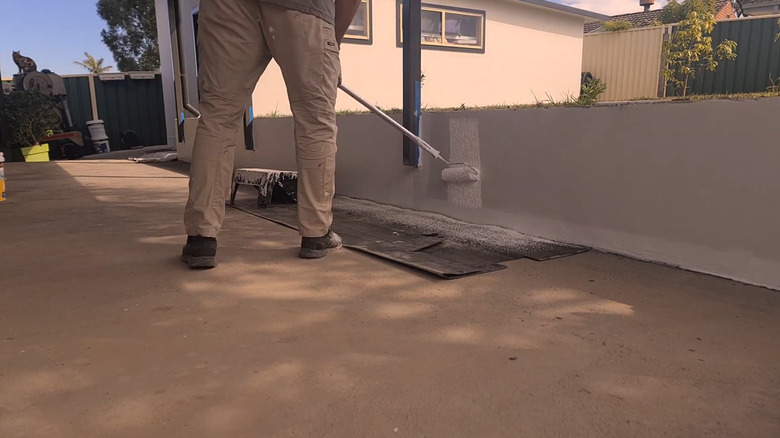 El rulosu ile beton istinat duvarını elastomerik boyayla boyayan kişi