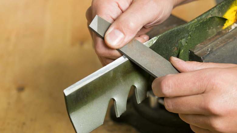 çim biçme makinesi bıçağı için metal dosya kullanan kişi