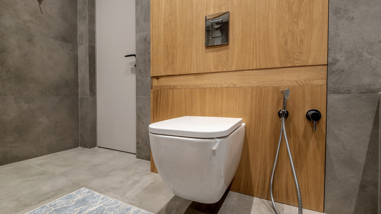 Modern bir banyoda ahşap bir duvara asılı, yanında bide bulunan minimalist bir tuvalet