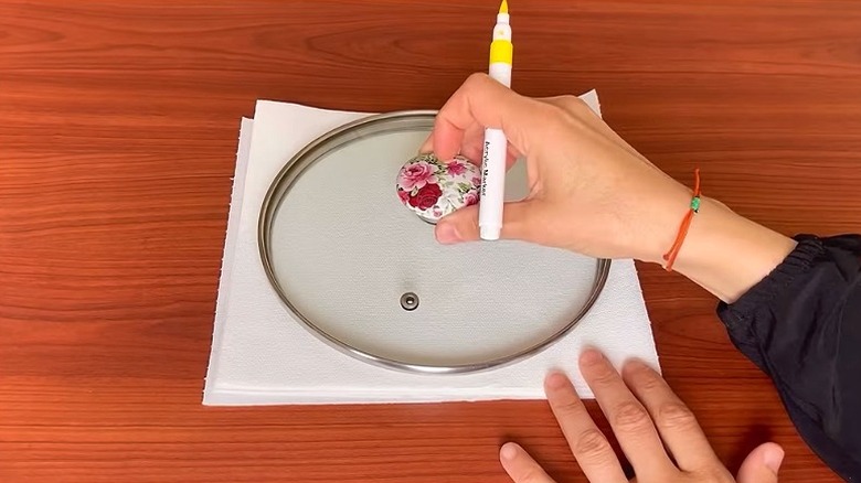 Katlanmış kağıt havluların üzerindeki tencere kapağını tutarken sarı bir kalem tutan bir kişinin ellerinin yakından görünümü