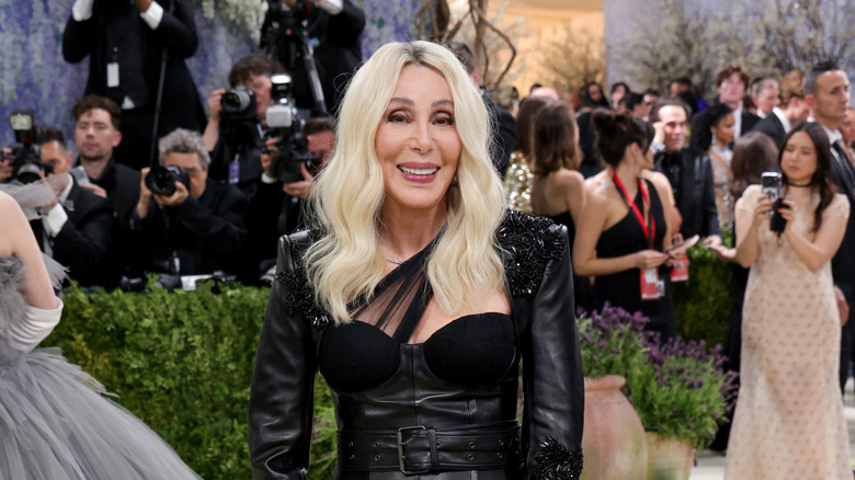 Cher, sarı saçlı ve siyah deri kıyafetiyle Met Gala'da halının üzerinde gülümsüyor