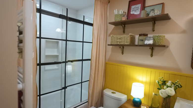tuvaletin arkasında sarı paneller ve cam duşu çevreleyen pembe perdelerle renkli küçük bir banyo makyajı