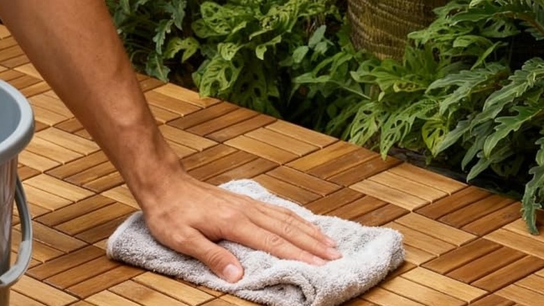 Arka planda bitkiler bulunan Thyoi ahşap döşemelerini kova ve bez kullanarak silen bir kişi