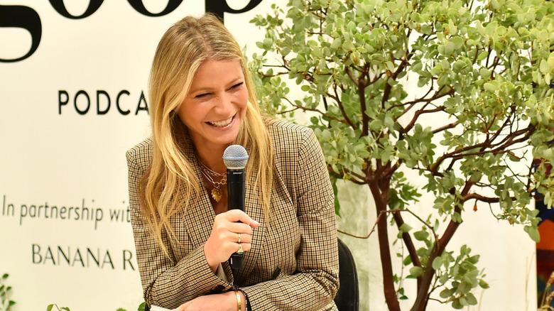 Gwyneth Paltrow ekose takım elbise ceketiyle bir Goop etkinliğinde mikrofona gülüyor