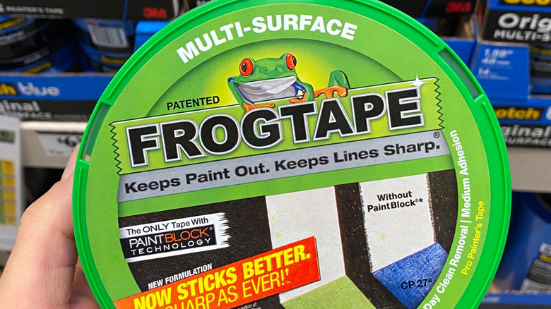 Bir el, bir hırdavat mağazası rafının önünde bir rulo yeşil FrogTape tutuyor.
