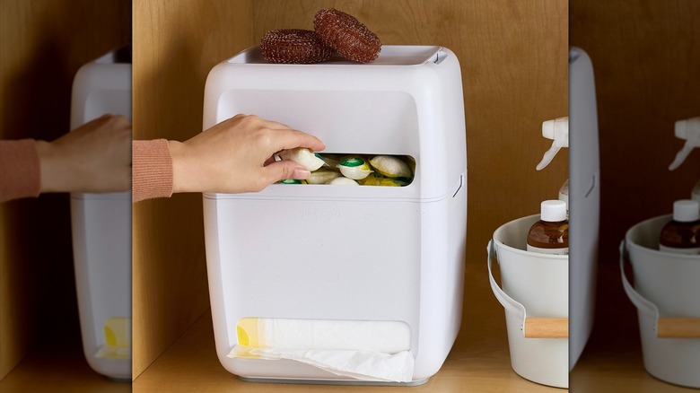 SinkSuite çöp torbasından ve bulaşık makinesi kapsülü dağıtıcısından bulaşık makinesi bölmesini çıkaran el
