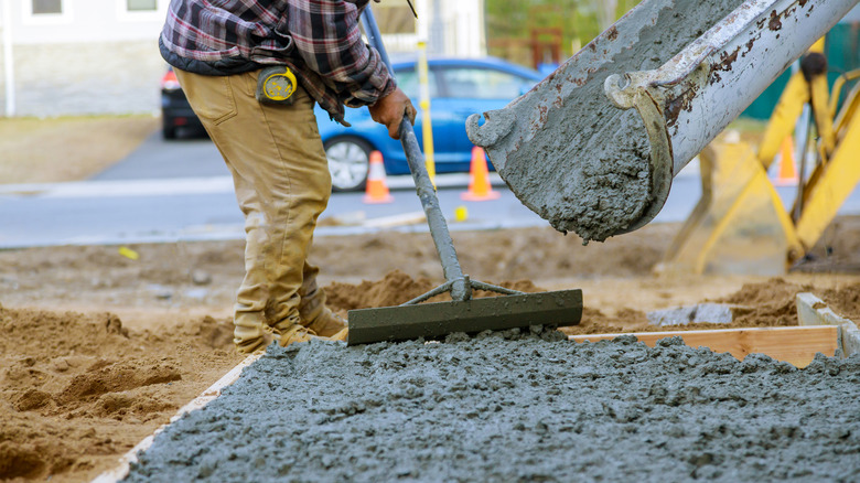 Çimento kamyonundan dökülen betonu düzelten inşaat işçisi.