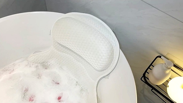 Baloncuklar ve gül yapraklarıyla dolu beyaz bir küvette beyaz bir banyo yastığı