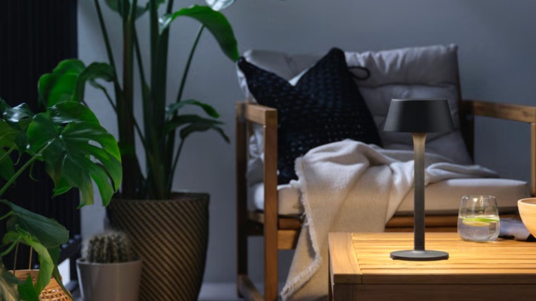Bitkilerle dolu bir balkon veya teras ve masanın üzerinde siyah IKEA portatif lamba