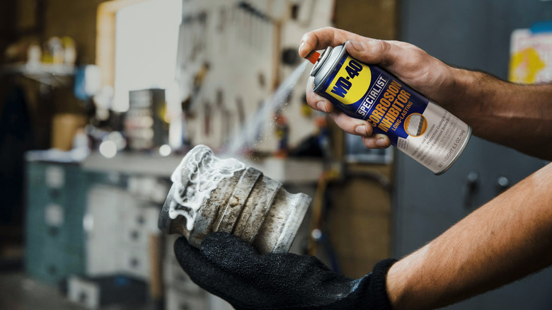metal bir bağlantı parçasına WD-40 sıkan kişi