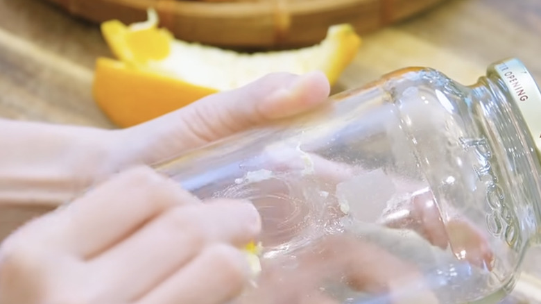 Bir kişi cam kavanozdaki çıkartma kalıntısını çıkarmak için limon kabuklarını kullanıyor.