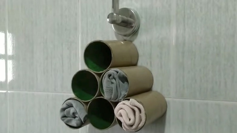 Tuvalet kağıdı tüplerinden yapılmış bir DIY paçavra organizatörü fayanslı bir duvarda asılı duruyor.
