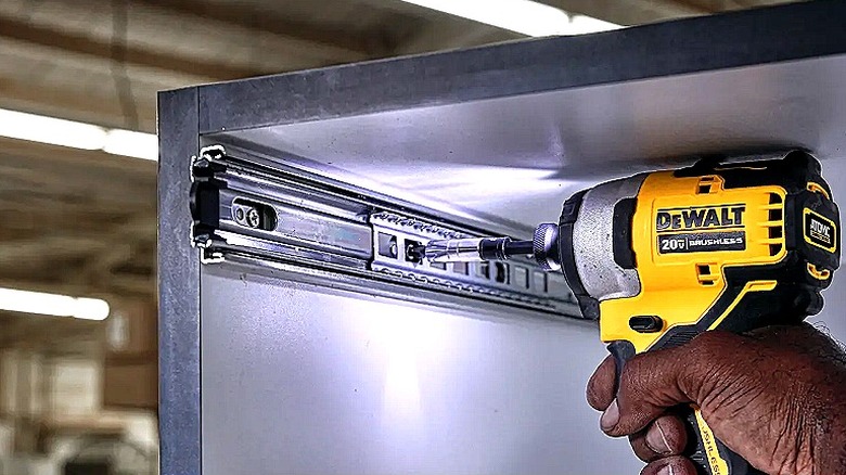 Sıkışık bir dolabın içine donanım kurmak için DeWalt darbeli sürücüyü kullanan bir el