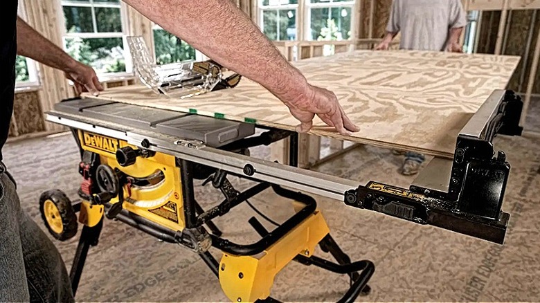 Bir çift işçi, DeWalt masa testeresini kullanırken bir kontrplak parçasını yerinde tutuyor