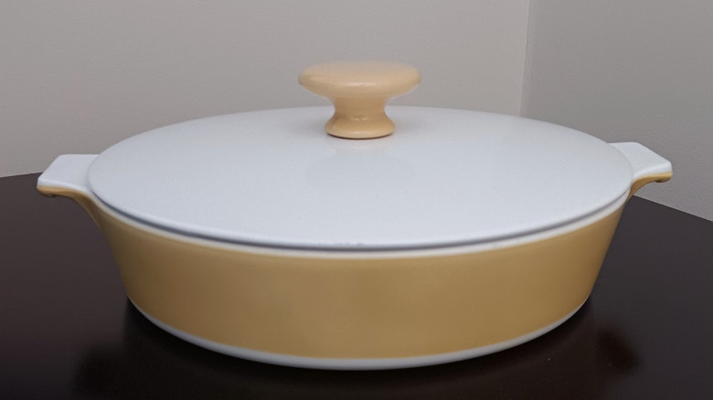 CorningWare'in karamela serisinden sarı bir tabak, beyaz bir kapak ve kapağın ortasında sarı bir düğme içeren bir tabak